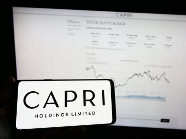 Stuttgart, Almanya - 06-17-2023: Moda şirketi Capri Holding Limited 'in logosuna sahip cep telefonu sahibi kişi iş sayfasının önünde ekranda görülüyor. Telefon ekranına odaklan.