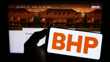 Stuttgart, Germany - 06-17-2023: Person holding smartphone with logo of Australian mining company BHP Group Limited on screen in front of website. Focus on phone display. clipart