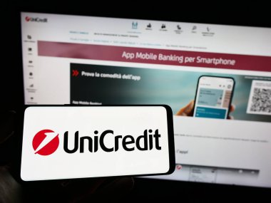 Stuttgart, Almanya - 06-17-2023: İtalyan finans şirketi UniCredit SpA 'nın logosuyla cep telefonu sahibi kişi iş sayfasının önünde ekranda. Telefon ekranına odaklan.