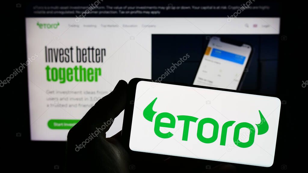 Stuttgart, Germany - 06-17-2023: Person holding smartphone with logo of Israeli social trading company eToro on screen in front of website. Focus on phone display.