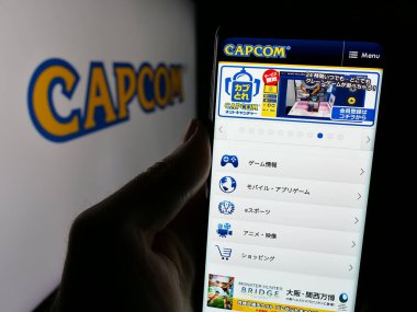 Stuttgart, Germany - 01-03-2024: Person holding mobile phone with website of Japanese video games company Capcom Co. Ltd. on screen with logo. Focus on center of phone display. clipart