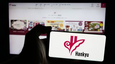 Stuttgart, Almanya - 01-03-2024: Japon demiryolu şirketi Hankyu Corporation 'ın logosuyla cep telefonu sahibi kişi iş sayfasının önünde ekranda. Telefon ekranına odaklan.