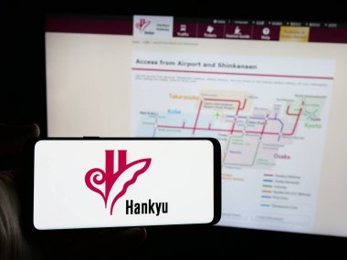 Stuttgart, Almanya - 01-03-2024: Japon demiryolu şirketi Hankyu Corporation 'ın logosunu elinde tutan kişi web sitesinin önünde ekranda. Telefon ekranına odaklan.