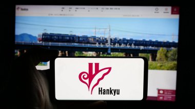 Stuttgart, Germany - 01-03-2024: Person holding cellphone with logo of Japanese railway company Hankyu Corporation on screen in front of business webpage. Focus on phone display. clipart