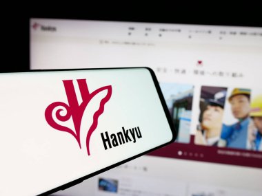 Stuttgart, Germany - 01-03-2024: Mobile phone with logo of Japanese railway company Hankyu Corporation on screen in front of business website. Focus on center of phone display. clipart