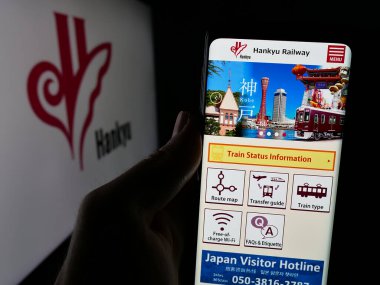 Stuttgart, Germany - 01-03-2024: Person holding cellphone with webpage of Japanese railway company Hankyu Corporation on screen in front of logo. Focus on center of phone display. clipart