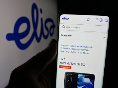 Stuttgart, Almanya - 01-03-2024: Fin telekomünikasyon şirketi Elisa Oyj 'un internet sayfası ile cep telefonu tutan kişi logonun önünde ekranda. Telefon ekranının merkezine odaklan.