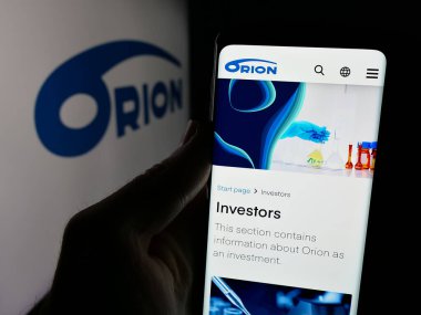 Stuttgart, Almanya - 01-03-2024: Fin ilaç şirketi Orion Oyj 'un internet sitesi ile cep telefonu elinde bulunan kişi logonun önünde ekranda. Telefon ekranının merkezine odaklan.