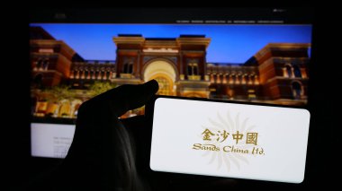 Stuttgart, Almanya - 01-03-2024: Konukseverlik şirketi Sands China Limited 'in logosunun bulunduğu cep telefonu sahibi kişi iş sayfasının önünde ekranda görülüyor. Telefon ekranına odaklan.