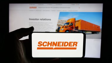 Stuttgart, Almanya - 01-07-2024: ABD 'li lojistik şirketi Schneider National Inc.' in logosuyla cep telefonu sahibi kişi iş sayfası önünde ekranda. Telefon ekranına odaklan.