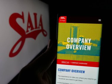 Stuttgart, Germany - 01-07-2024: Person holding cellphone with webpage of US trucking company Saia Inc. on screen in front of business logo. Focus on center of phone display. clipart