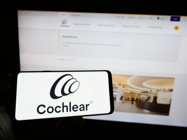 Stuttgart, Almanya - 04-02-2023: Üzerinde tıbbi teknoloji şirketi Cochlear Limited 'in logosu olan cep telefonu sahibi kişi iş sayfasının önünde ekranda. Telefon ekranına odaklan.