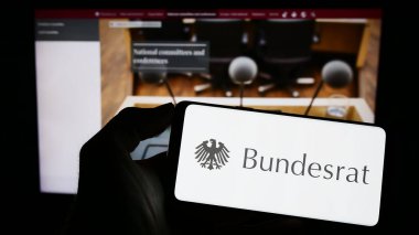 Stuttgart, Germany - 04-02-2023: Person holding cellphone with seal of German legislative body Bundesrat on screen in front of webpage. Focus on phone display. clipart