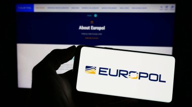 Stuttgart, Germany - 04-02-2023: Person holding cellphone with logo of EU law enforcement agency Europol on screen in front of webpage. Focus on phone display. clipart