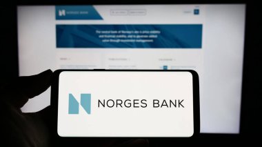 Stuttgart, Almanya - 04-02-2023: Web sitesinin önünde Norges Bank 'ın logosunun bulunduğu akıllı telefonu elinde tutan kişi. Telefon ekranına odaklan.