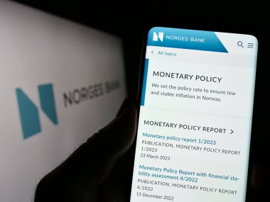 Stuttgart, Germany - 04-02-2023: Person holding cellphone with webpage of Norwegian central bank Norges Bank on screen in front of logo. Focus on center of phone display. clipart