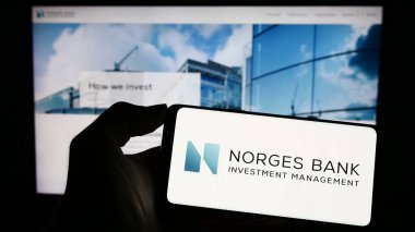 Stuttgart, Germany - 04-02-2023: Person holding cellphone with logo of Norges Bank Investment Management (NBIM) on screen in front of webpage. Focus on phone display. clipart