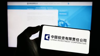 Stuttgart, Almanya - 04-02-2023: İnternet sayfası önünde Çin Yatırım Şirketi 'nin (CIC) logosuyla cep telefonu tutan kişi. Telefon ekranına odaklan.