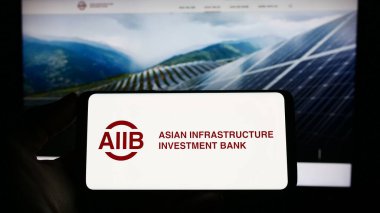 Stuttgart, Almanya - 04-02-2023: Web sitesi önünde Asya Altyapı Yatırım Bankası 'nın (AIIB) logosuna sahip akıllı telefonu elinde tutan kişi. Telefon ekranına odaklan.