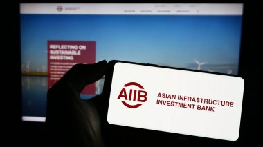Stuttgart, Almanya - 04-02-2023: Web sayfası önünde Asya Altyapı Yatırım Bankası (AIIB) logosu olan cep telefonu sahibi kişi. Telefon ekranına odaklan.