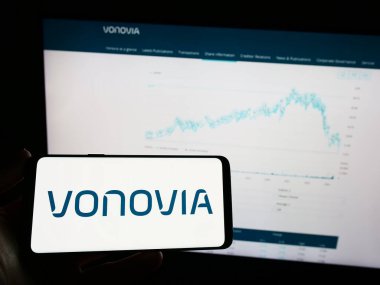 Stuttgart, Almanya - 04-04-2023: Alman emlak şirketi Vonovia SE 'nin logosuna sahip cep telefonu sahibi kişi iş sayfasının önünde ekranda. Telefon ekranına odaklan.