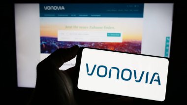 Stuttgart, Almanya - 04-04-2023: Alman emlak şirketi Vonovia SE 'nin logosuyla cep telefonu sahibi kişi iş sayfasının önünde ekranda. Telefon ekranına odaklan.