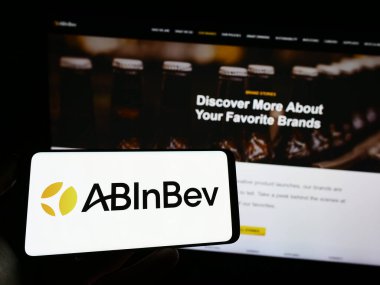 Stuttgart, Almanya - 04-04-2023: Web sayfası önünde bira şirketi Anheuser-Busch InBev 'in (AB InBev) logosunun bulunduğu cep telefonu sahibi kişi. Telefon ekranına odaklan.