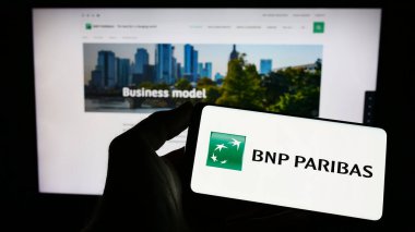 Stuttgart, Almanya - 04-04-2023: Fransız bankacılık şirketi BNP Paribas S.A. 'nın logosuyla cep telefonu sahibi kişi iş sayfasının önünde ekranda. Telefon ekranına odaklan.