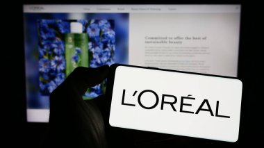 Stuttgart, Almanya - 04-04-2023: Fransız özel bakım şirketi L 'Oreal SA' nın logosuyla cep telefonu sahibi kişi iş sayfasının önünde ekranda. Telefon ekranına odaklan.