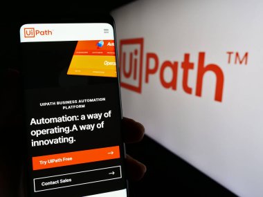 Stuttgart, Germany - 04-04-2023: Person holding cellphone with web page of automation software company UiPath Inc. on screen in front of logo. Focus on center of phone display. clipart