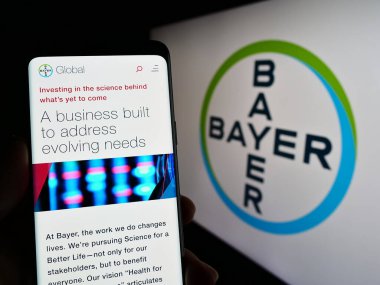 Stuttgart, Almanya - 04-16-2023: Alman ilaç firması Bayer AG 'nin internet sayfası olan akıllı telefon sahibi kişi logonun önünde ekranda. Telefon ekranının merkezine odaklan.