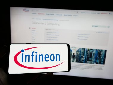 Stuttgart, Almanya - 04-16-2023: Yarı iletken firma Infineon Technologies AG 'nin logosuna sahip akıllı telefon sahibi kişi web sitesinin önünde ekranda. Telefon ekranına odaklan.