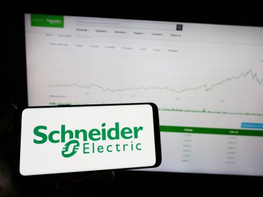 Stuttgart, Almanya - 04-16-2023: Fransız Schneider Electric SE şirketinin logosunun bulunduğu cep telefonu sahibi kişi iş sayfasının önünde ekranda. Telefon ekranına odaklan.