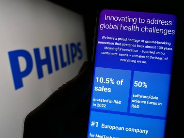 Stuttgart, Almanya - 04-16-2023: Hollandalı Koninklijke Philips NV şirketinin web sayfası ile logo önünde cep telefonu tutan kişi. Telefon ekranının merkezine odaklan.