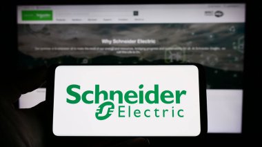 Stuttgart, Almanya - 04-16-2023: Fransız Schneider Electric SE şirketinin logosuyla cep telefonu sahibi kişi iş sayfasının önünde ekranda. Telefon ekranına odaklan.