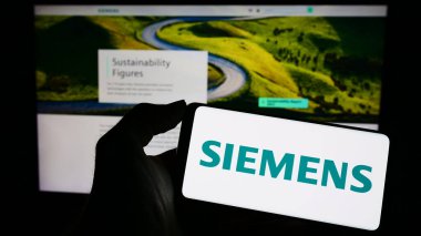 Stuttgart, Almanya - 04-16-2023: Alman holdingi Siemens AG 'nin logosunun bulunduğu cep telefonu sahibi kişi iş sayfasının önünde ekranda. Telefon ekranına odaklan.