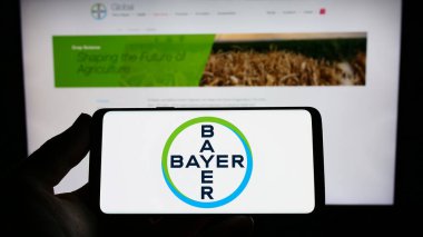 Stuttgart, Germany - 04-16-2023: Person holding smartphone with logo of German pharmaceutical company Bayer AG on screen in front of website. Focus on phone display. clipart