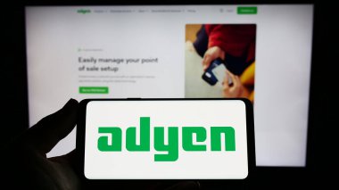 Stuttgart, Almanya - 04-16-2023: Hollandalı ödeme şirketi Adyen NV 'nin logosuna sahip akıllı telefon sahibi kişi web sitesinin önünde ekranda. Telefon ekranına odaklan.