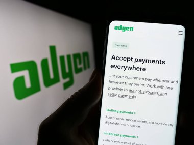 Stuttgart, Almanya - 04-16-2023: Hollandalı ödeme şirketi Adyen N.V. 'nin internet sayfası ile cep telefonu tutan kişi iş logosu önünde ekranda. Telefon ekranının merkezine odaklan.