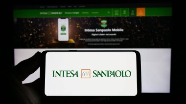 Stuttgart, Germany - 04-16-2023: Person holding smartphone with logo of Italian banking company Intesa Sanpaolo S.p.A. on screen in front of website. Focus on phone display. clipart