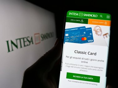 Stuttgart, Almanya - 04-16-2023: İtalyan bankacılık şirketi Intesa Sanpaolo SpA 'nın logolu web sayfası ile akıllı telefon tutan kişi. Telefon ekranının merkezine odaklan.