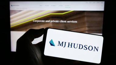 Stuttgart, Almanya - 04-19-2023: İngiliz finans şirketi MJ Hudson Group 'un logosunun bulunduğu cep telefonu web sayfası önünde ekranda. Telefon ekranına odaklan.
