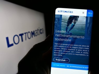 Stuttgart, Almanya - 04-19-2023: İtalyan kumar şirketi Lottomatica S.P.A. 'nın internet sitesi ile akıllı telefonu elinde tutan kişi logolu ekranda. Telefon ekranının merkezine odaklan.