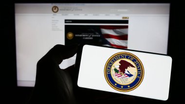 Stuttgart, Germany - 04-19-2023: Person holding mobile phone with seal of United States Department of Justice (DOJ) on screen in front of web page. Focus on phone display.