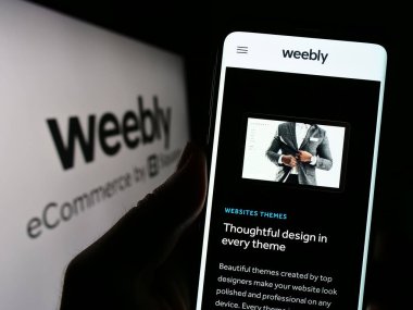 Stuttgart, Almanya - 04-19-2023: Web sunucu şirketi Weebly 'nin web sayfası ile cep telefonu tutan kişi iş logosu önünde ekranda. Telefon ekranının merkezine odaklan.