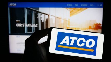 Stuttgart, Almanya - 04-19-2023: Kanadalı enerji şirketi ATCO Ltd. 'nin logosuna sahip cep telefonu sahibi kişi iş sayfasının önünde ekranda. Telefon ekranına odaklan.