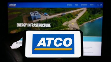 Stuttgart, Almanya - 04-19-2023: Kanadalı enerji şirketi ATCO Ltd. 'nin logosuyla cep telefonu sahibi kişi iş sayfasının önünde ekranda. Telefon ekranına odaklan.