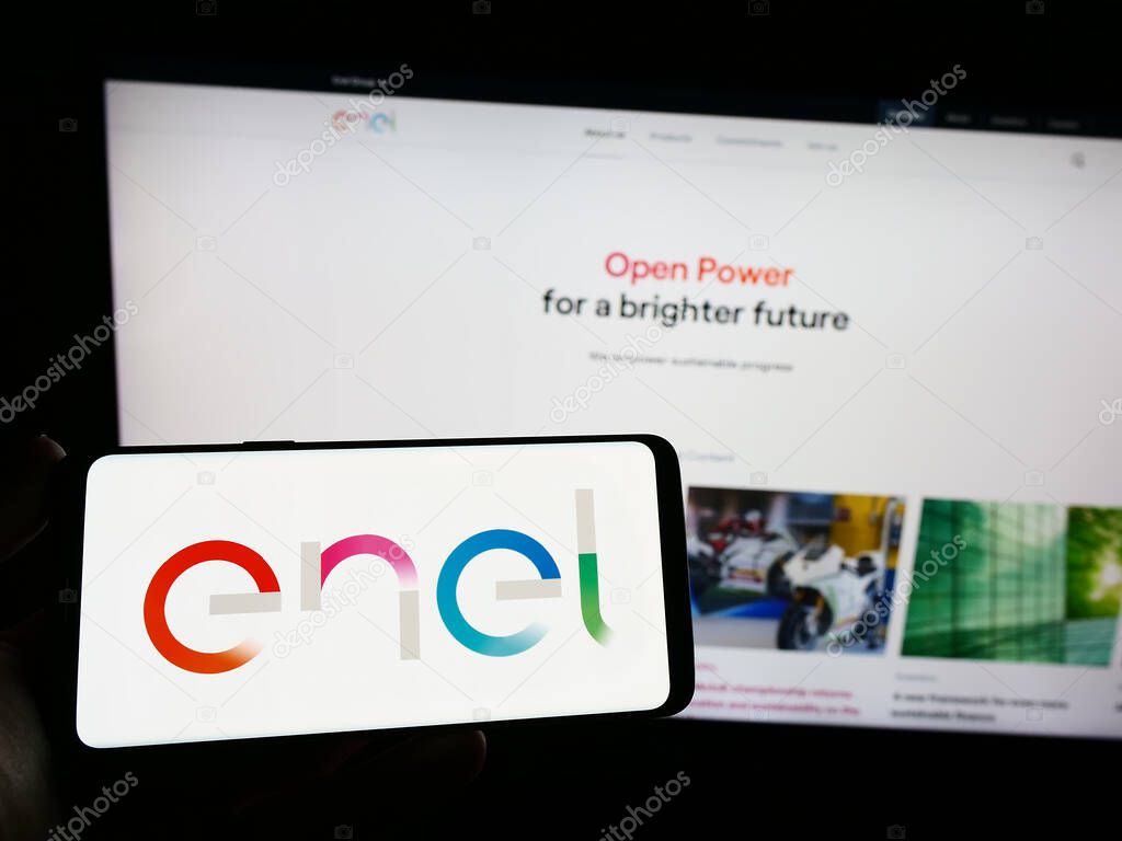 Stuttgart, Germany - 04-16-2023: Person holding smartphone with logo of Italian utility company Enel S.p.A. on screen in front of website. Focus on phone display.