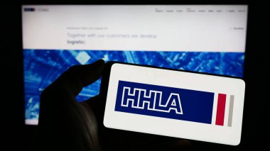 Stuttgart, Almanya - 04-20-2023: Web sitesi önünde Hamburger Hafen und Logistik AG (HHLA) şirketinin logosuna sahip akıllı telefon sahibi kişi. Telefon ekranına odaklan.