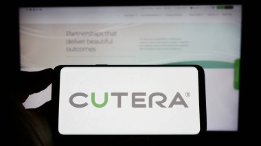 Stuttgart, Almanya - 04-20-2023: ABD 'li tıbbi teknoloji şirketi Cutera Inc.' nin logosuyla cep telefonu sahibi kişi iş sayfasının önünde ekranda. Telefon ekranına odaklan.